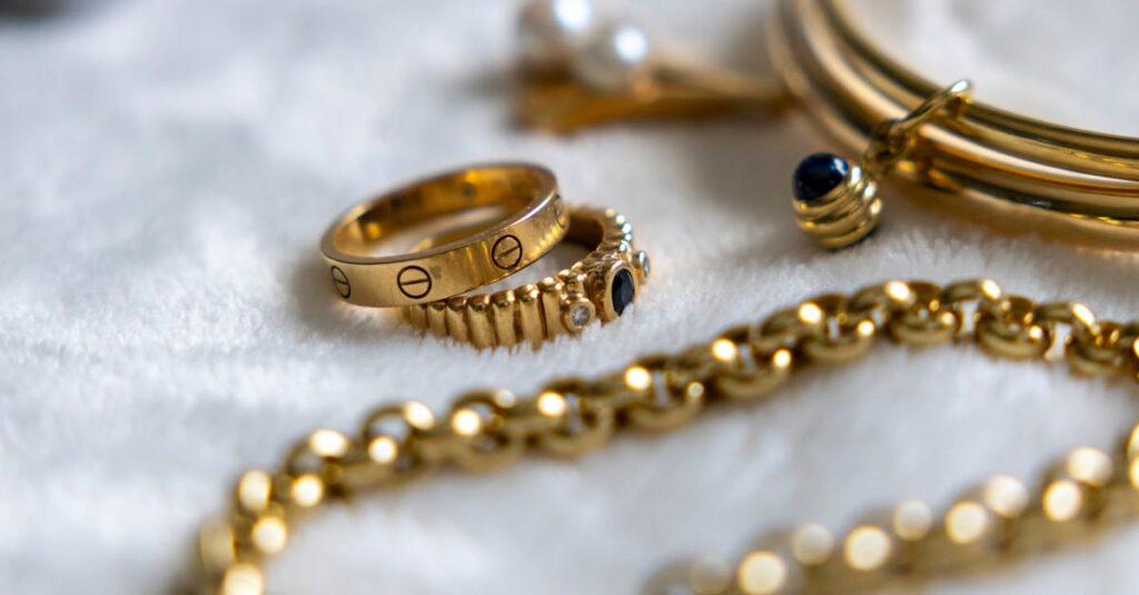 Collection of gold rings, bracelets, and chains with gemstones on a textured surface.